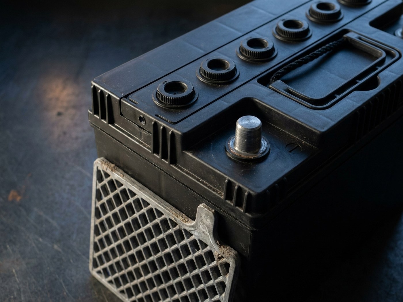 Top of an unmarked battery with a row of removable vent caps and a cast lead grid plate